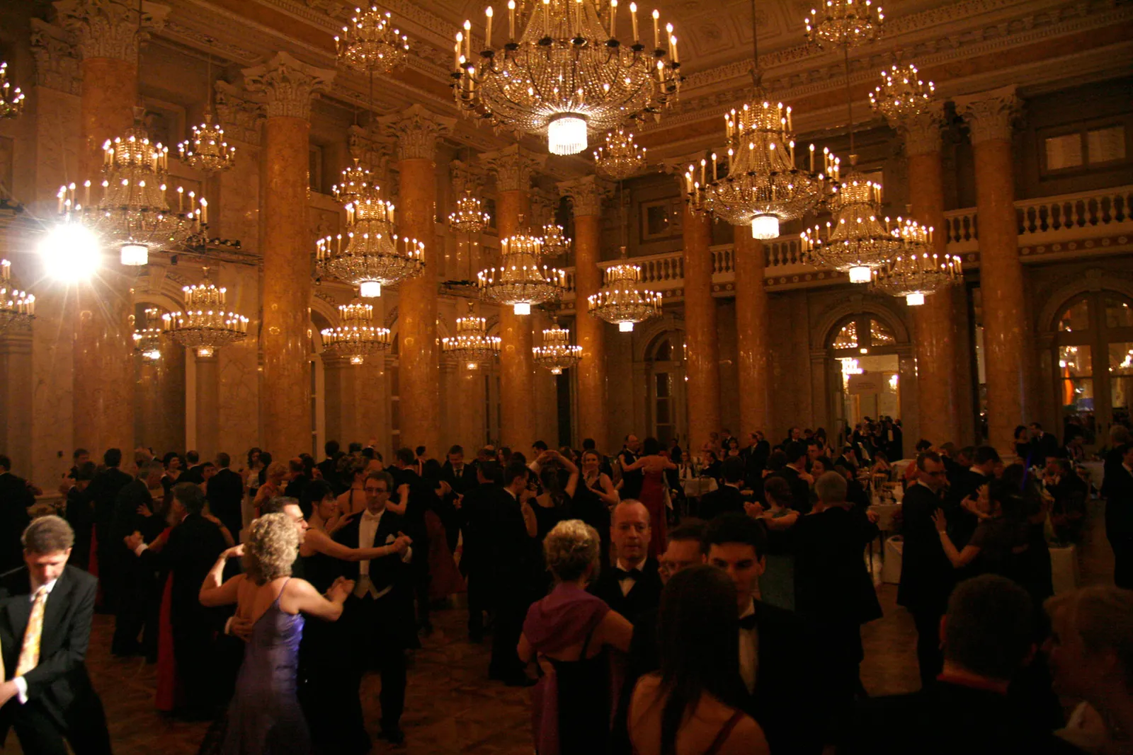 The Ceremonial Hall of the Hofburg during a ball, with tall marble columns, many chandeliers and dancing couples