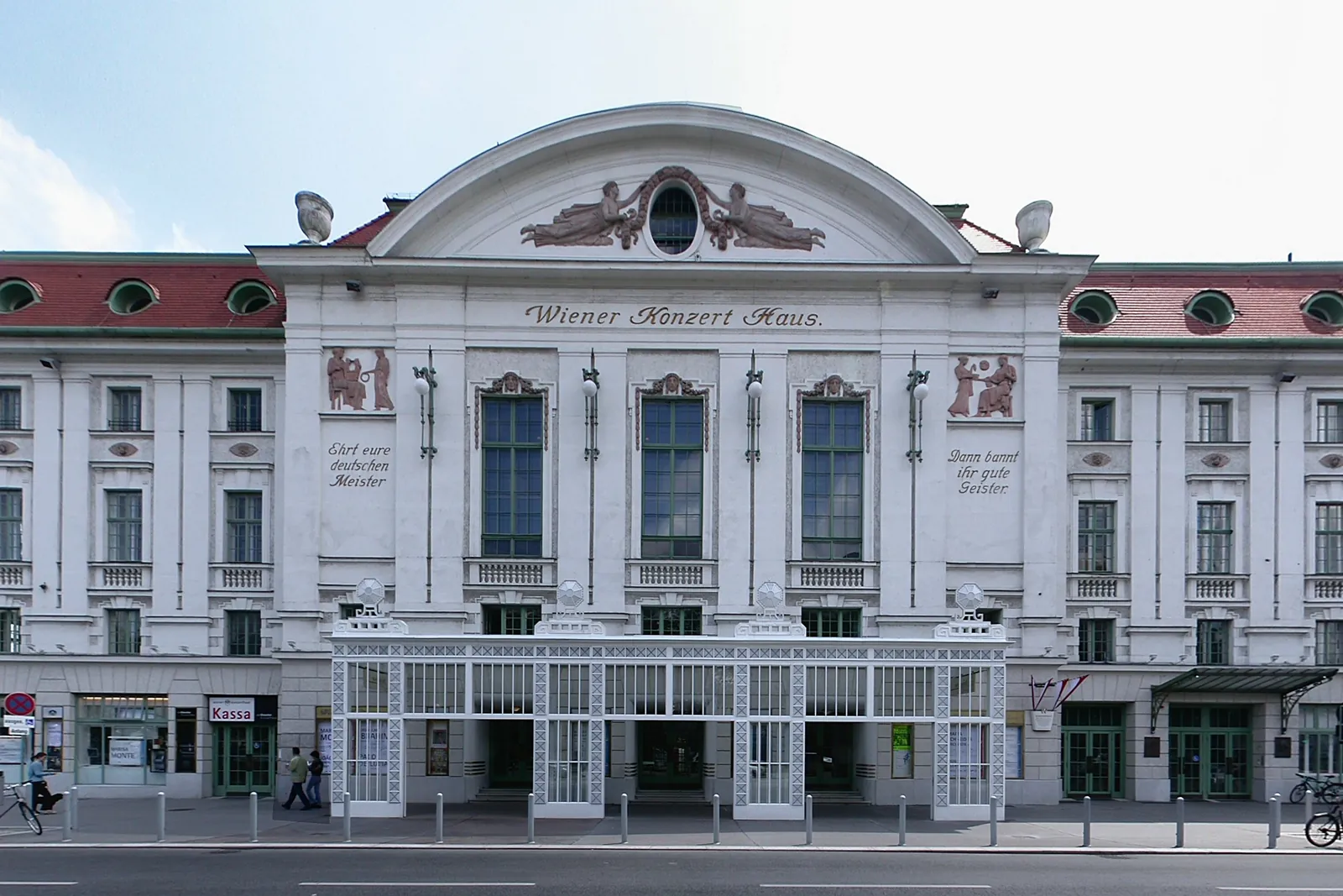 The white street front of the Wiener Konzerthaus, with a red tiled roof and a glass and iron porch over the entrances